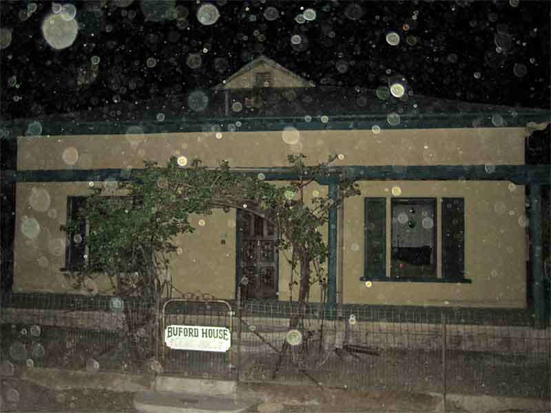 Nighttime view of Buford House with orbs visible in front of the building. The building's facade, arched entryway, and illuminated windows are visible through the orbs.