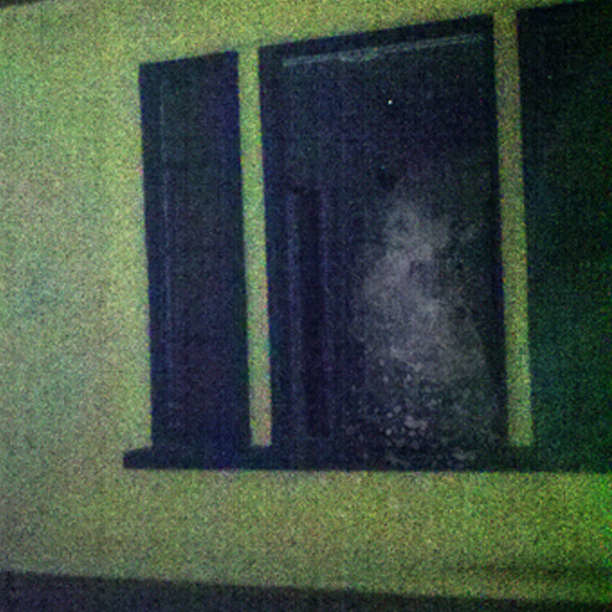 Dark window at night with a hazy, light-colored shape visible inside, giving an eerie or mysterious appearance.