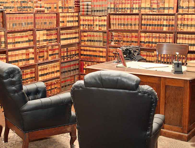 Reconstructed 19th-century lawyer's office in the Tombstone Courthouse Museum. The room features floor-to-ceiling bookshelves filled with leather-bound law books, a wooden desk with a vintage typewriter, and two black leather armchairs. This exhibit recreates the atmosphere of a period legal office, showcasing the tools and resources of frontier justice.