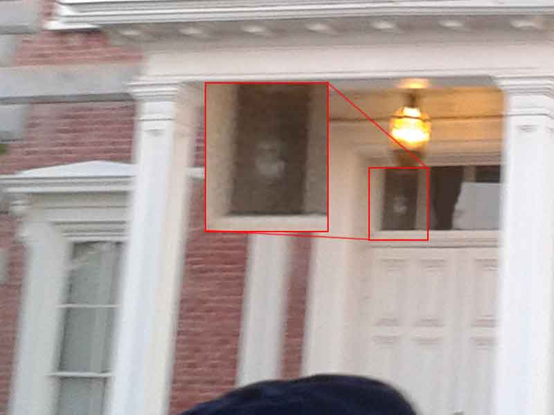 Exterior view of the Tombstone Courthouse with two red boxes highlighting windows. In each box, there appears to be a faint, ghostly face visible, suggesting potential paranormal activity. The image is slightly blurry, typical of amateur ghost photography.