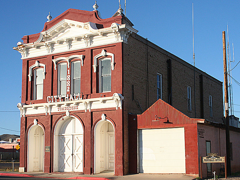 Historic Tombstone City Hall building with ornate red and white facade. Two-story structure featuring arched doorways, tall windows, and decorative cornices. The front reads 