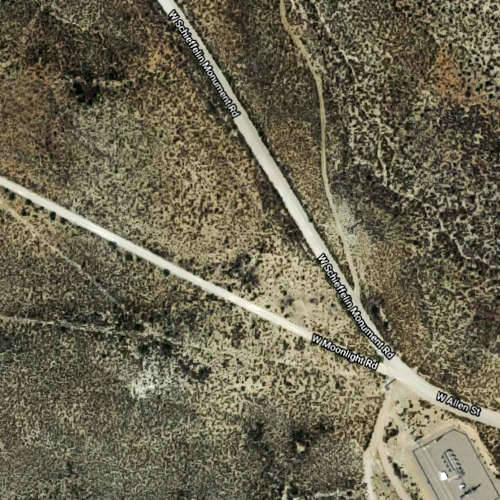 Aerial view of desert terrain showing intersecting gravel roads. Three main paths visible: a wider road diagonally from bottom right, a thinner branch to the left, and another from top left. Sparse vegetation and an electric substation visible. Road names are partially shown.