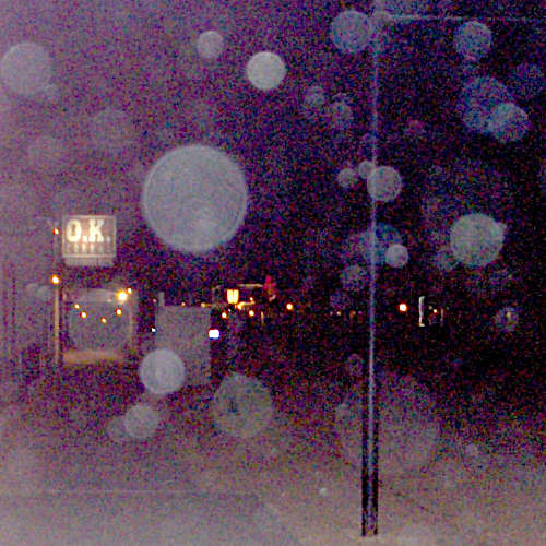 Nighttime street scene with 'O.K. Corral' sign visible, illuminated lights, and floating orbs in the foreground.