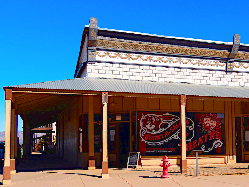 Historic Western-style building with ornate facade, covered wooden porch, and theater signage. Red fire hydrant visible in foreground.